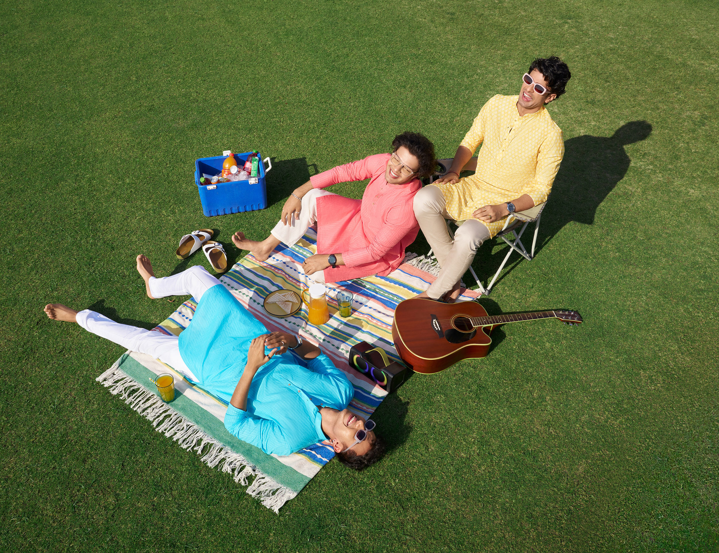 Three friends relax on a picnic blanket in a park, enjoying conversation, snacks, and a sunny outdoor gathering.
